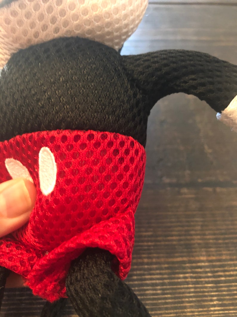 May include: Red, black, and white plush toy shaped like Mickey Mouse. The toy is made of a mesh material and has a red, white, and black design.