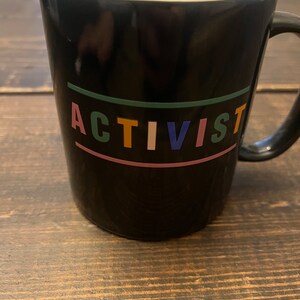 May include: Black ceramic mug with the word "ACTIVIST" written in colorful letters on the front.