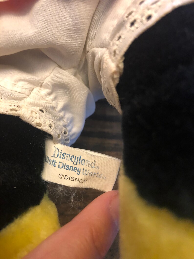 K&ouml;nnte beinhalten: Ein wei&szlig;es Etikett mit schwarzem Text, auf dem "Disneyland Walt Disney World &copy;DISNEY" steht, das an einem schwarzen und gelben Pl&uuml;schtier befestigt ist.
