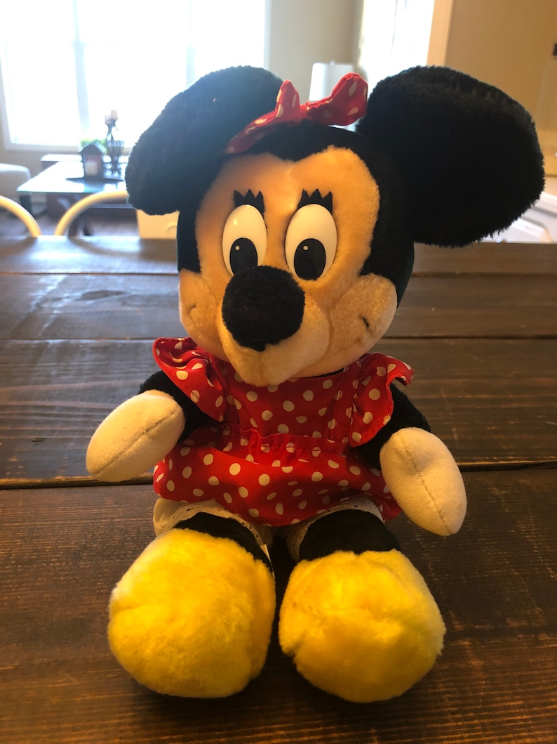 K&ouml;nnte beinhalten: Ein Pl&uuml;schtier von Minnie Mouse, das ein rotes Kleid mit wei&szlig;en Punkten und eine rote Schleife tr&auml;gt. Sie hat schwarze Ohren und eine schwarze Nase, und ihre Augen sind gro&szlig; und wei&szlig;.