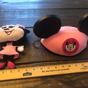 May include: Pink Minnie Mouse ears with a black felt headband and a pink felt Minnie Mouse head with a Walt Disney World logo on the front.