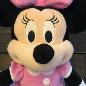 May include: A pink plush Minnie Mouse toy with white polka dots on her dress and bow. She has black ears, a black nose, and embroidered eyes and eyelashes.