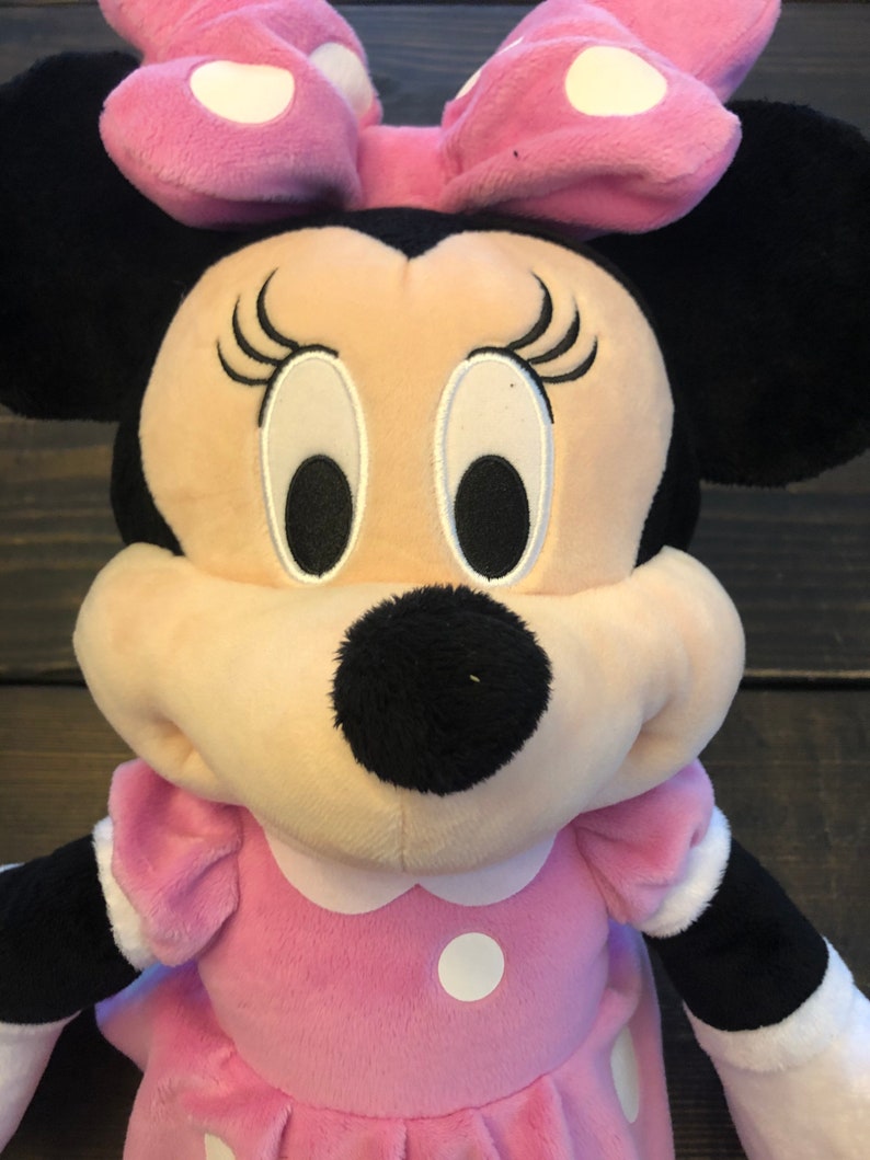 May include: A pink plush Minnie Mouse toy with white polka dots on her dress and bow. She has black ears, a black nose, and embroidered eyes and eyelashes.