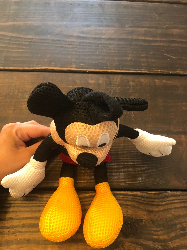 May include: A black and yellow mesh Mickey Mouse plush toy. The toy has a red shirt and large black ears.