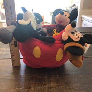 Peut inclure: Quatre personnages en peluche de Mickey Mouse, dont un Mickey noir et blanc classique, un Mickey rouge et jaune, un Mickey violet et un Mickey brun, sont tous assis dans une t&ecirc;te de Mickey Mouse en peluche rouge.