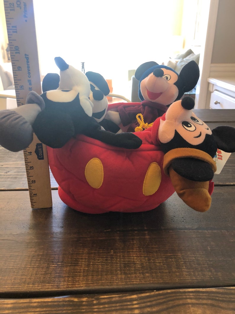 Peut inclure: Quatre personnages en peluche de Mickey Mouse, dont un Mickey noir et blanc classique, un Mickey rouge et jaune, un Mickey violet et un Mickey brun, sont tous assis dans une t&ecirc;te de Mickey Mouse en peluche rouge.