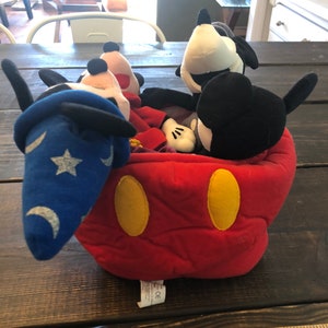 Peut inclure: Une t&ecirc;te de Mickey Mouse en peluche rouge avec des oreilles jaunes et des yeux noirs. &Agrave; l'int&eacute;rieur de la t&ecirc;te se trouvent quatre personnages de Mickey Mouse en peluche, dont Mickey Mouse en magicien avec un chapeau bleu et une &eacute;toile.