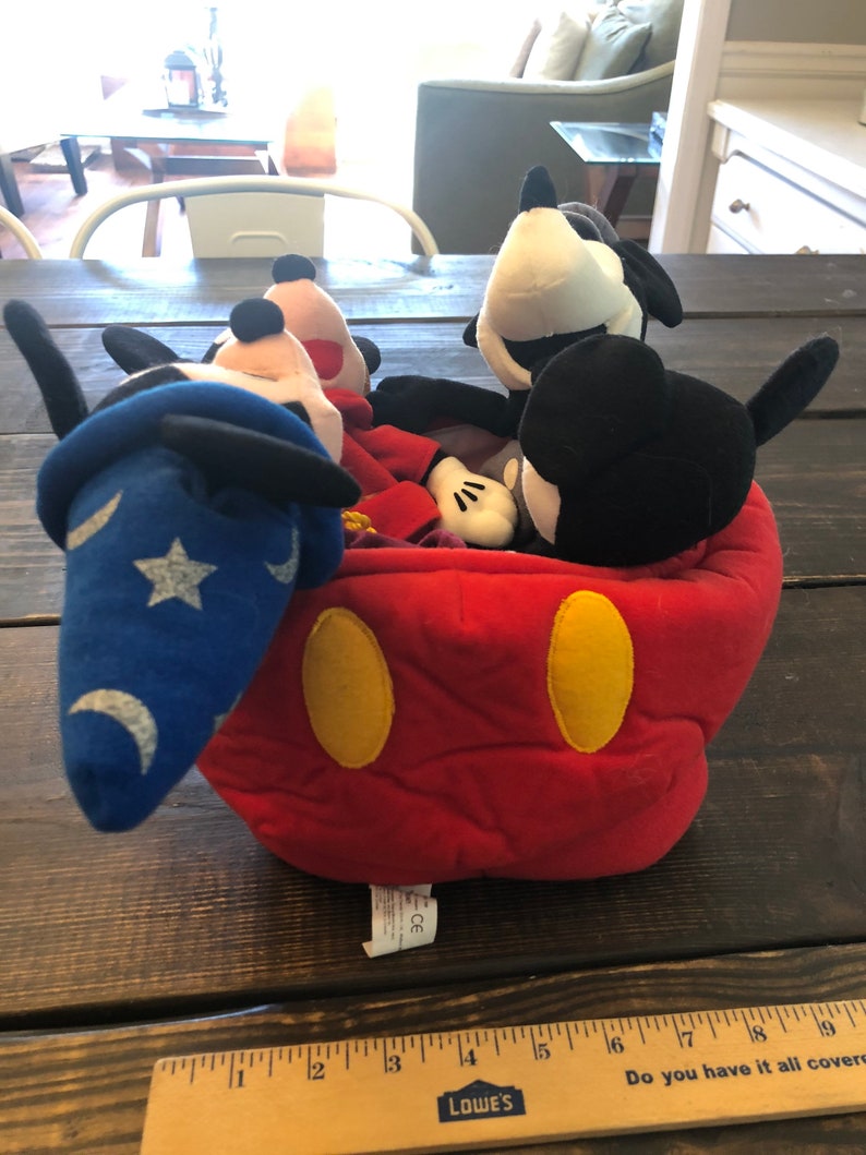 Peut inclure: Une t&ecirc;te de Mickey Mouse en peluche rouge avec des oreilles jaunes et des yeux noirs. &Agrave; l'int&eacute;rieur de la t&ecirc;te se trouvent quatre personnages de Mickey Mouse en peluche, dont Mickey Mouse en magicien avec un chapeau bleu et une &eacute;toile.