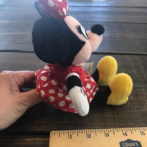 Puede incluir: Un vestido rojo con lunares blancos y una cabeza de peluche de Minnie Mouse en blanco y negro. El peluche est&aacute; sentado sobre una superficie de madera con una regla.