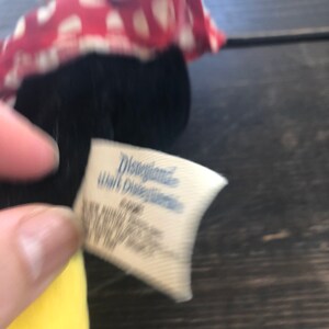 Puede incluir: Primer plano de un juguete de peluche vintage de Disney con un vestido de lunares rojos y blancos. La etiqueta dice "Disneyland Walt Disney World".