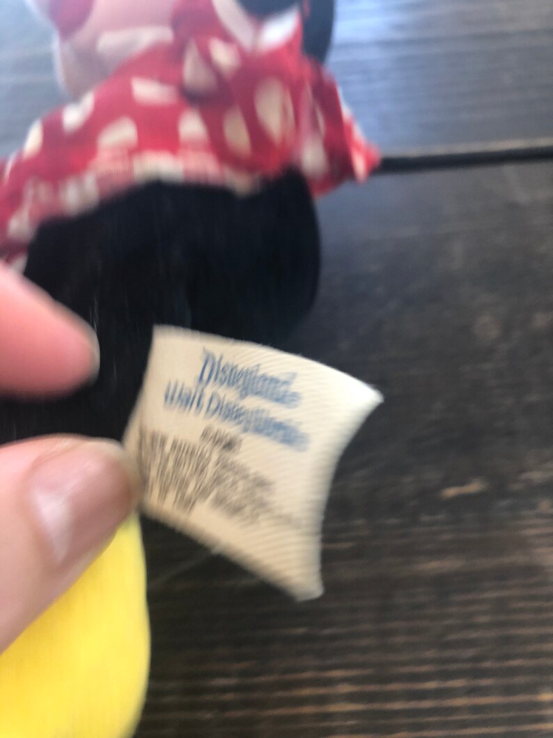 Puede incluir: Primer plano de un juguete de peluche vintage de Disney con un vestido de lunares rojos y blancos. La etiqueta dice "Disneyland Walt Disney World".