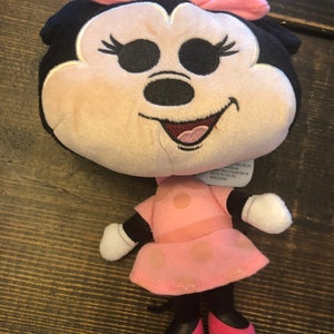 May include: Pink and black plush toy of Minnie Mouse with a pink bow and polka dot dress. The toy is about 10 inches tall.
