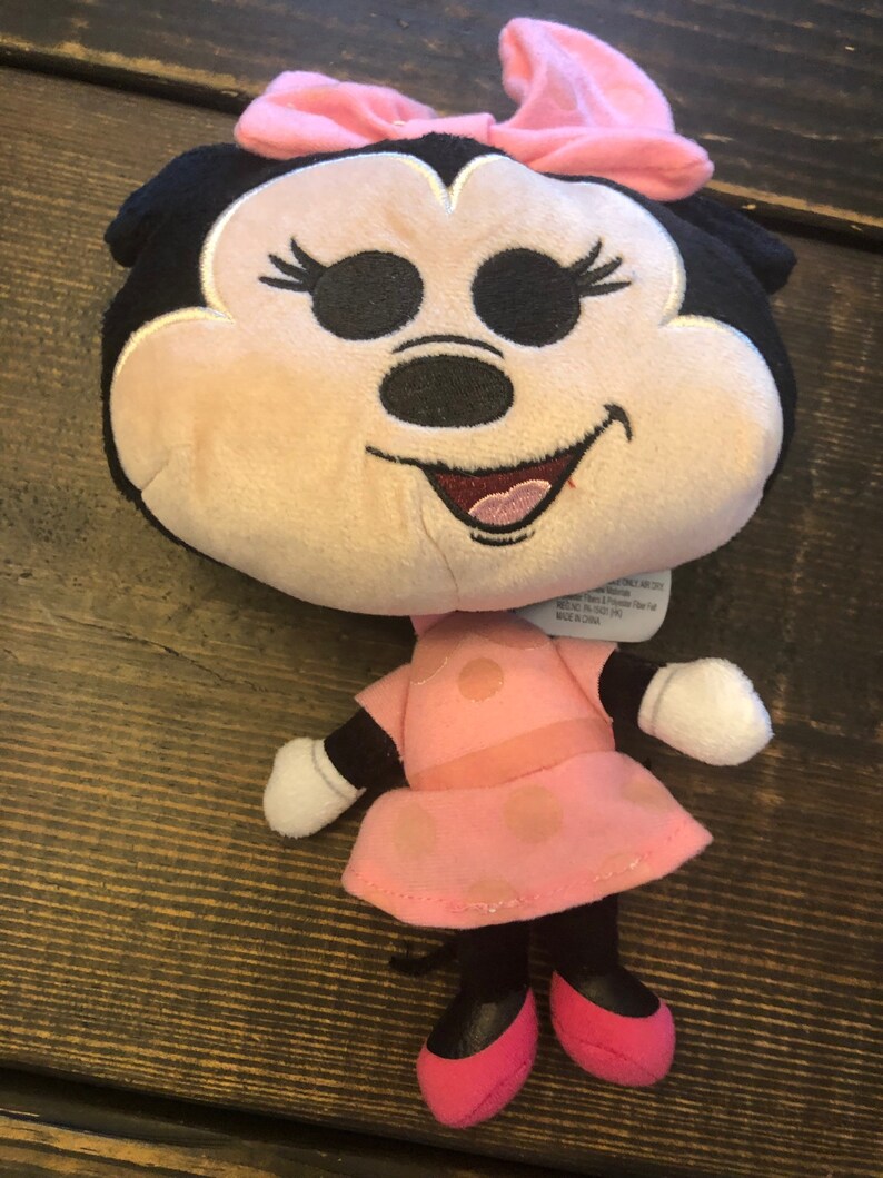 May include: Pink and black plush toy of Minnie Mouse with a pink bow and polka dot dress. The toy is about 10 inches tall.
