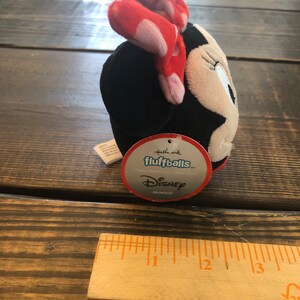 Op de afbeelding: Een zwart en wit pluche speelgoed van Minnie Mouse met een rode strik met witte stippen. Het speelgoed is gelabeld "Hallmark fluffballs Disney Minnie".