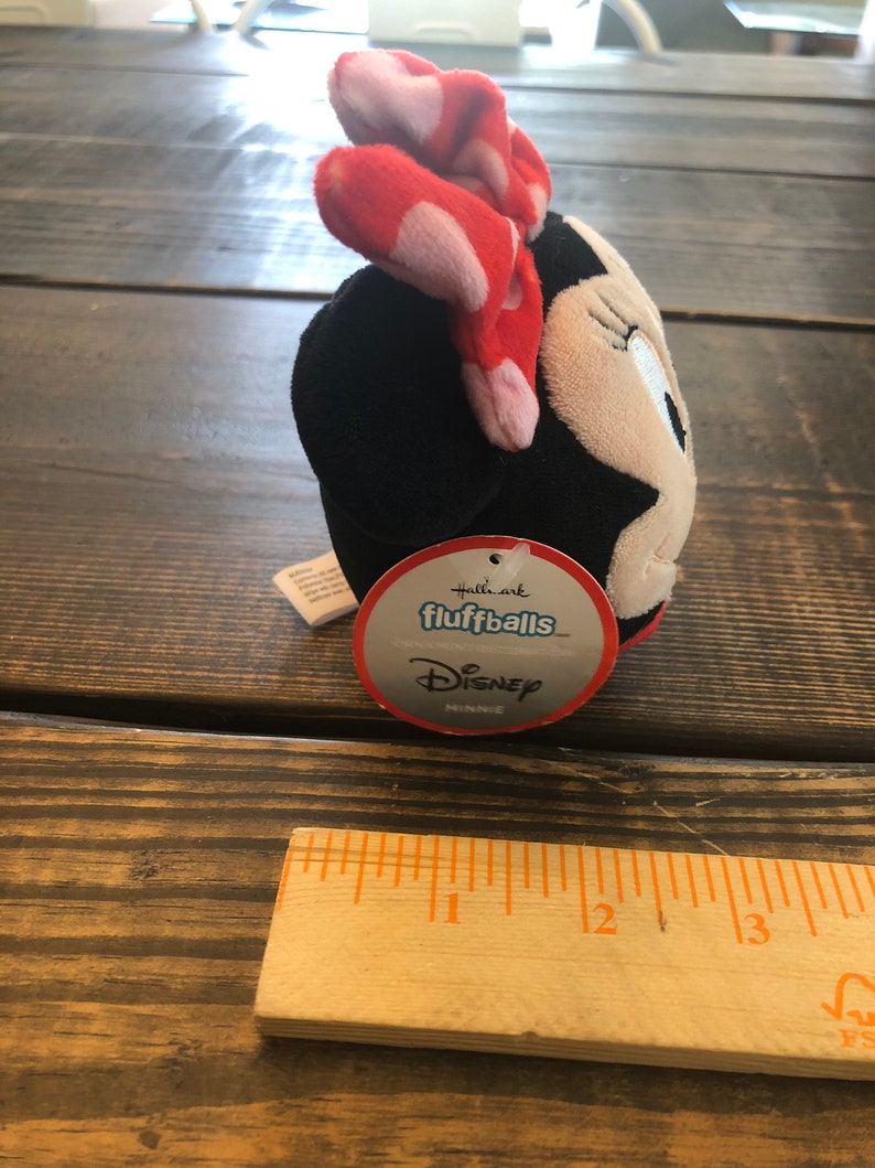 Op de afbeelding: Een zwart en wit pluche speelgoed van Minnie Mouse met een rode strik met witte stippen. Het speelgoed is gelabeld "Hallmark fluffballs Disney Minnie".