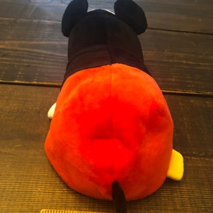 May include: A plush toy of Mickey Mouse in his signature red shorts and yellow shoes. The toy is lying on its back with its tail visible. The toy is approximately 4 inches long.