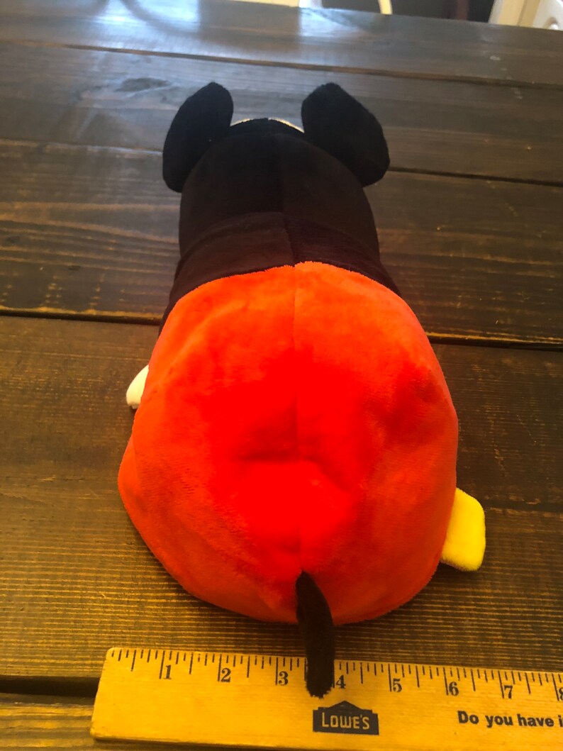 May include: A plush toy of Mickey Mouse in his signature red shorts and yellow shoes. The toy is lying on its back with its tail visible. The toy is approximately 4 inches long.