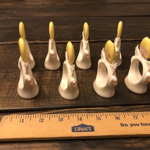 Puede incluir: Conjunto de siete anillos de servilleta de cer&aacute;mica blanca con un dise&ntilde;o de &aacute;ngel amarillo. Cada anillo tiene un halo amarillo y una cara rosa.