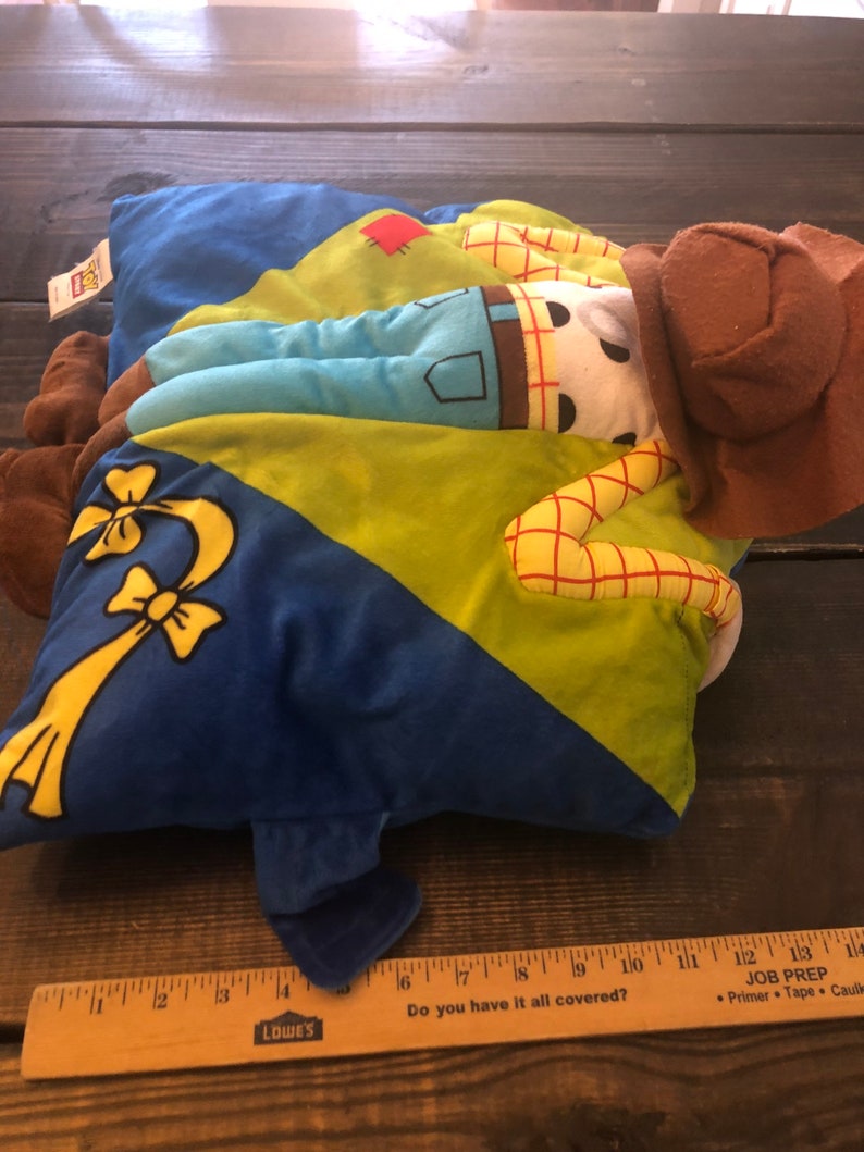 以下が含まれることがあります： トイストーリーのキャラクターが描かれた青、緑、黄色のぬいぐるみ枕。キャラクターは茶色のカウボーイハットをかぶって横になっています。枕の長さは約17インチです。