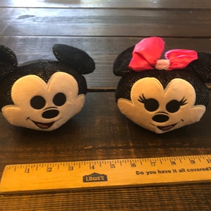 May include: Black and white plush Mickey Mouse and Minnie Mouse heads with sparkly details. Minnie Mouse has a pink bow.