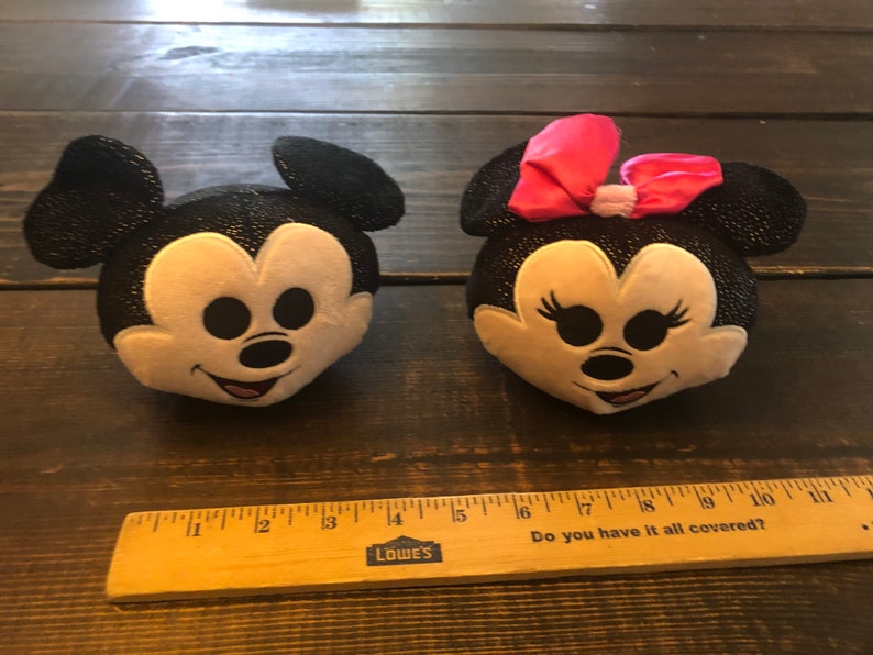 May include: Black and white plush Mickey Mouse and Minnie Mouse heads with sparkly details. Minnie Mouse has a pink bow.
