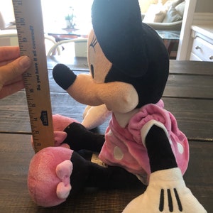 May include: A pink and black plush Minnie Mouse toy with white polka dots on her dress. She is sitting with her legs crossed and her arms outstretched. The toy is about 17 inches tall.