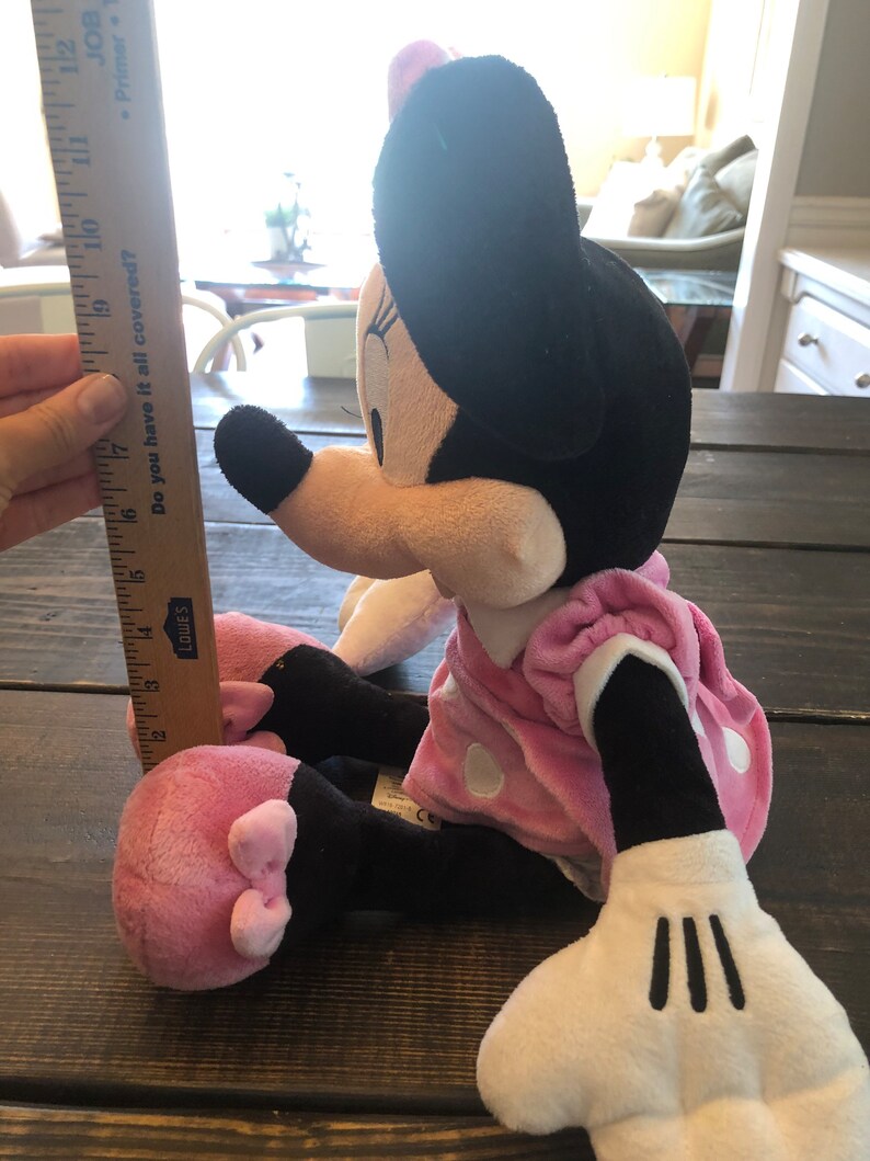 May include: A pink and black plush Minnie Mouse toy with white polka dots on her dress. She is sitting with her legs crossed and her arms outstretched. The toy is about 17 inches tall.