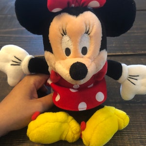 May include: A plush toy of Minnie Mouse with a red and white polka dot dress, a red bow with white polka dots, and yellow shoes.