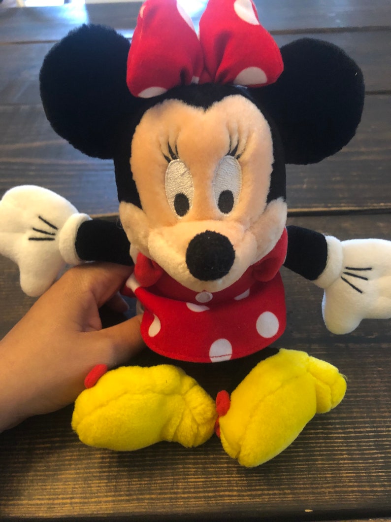 May include: A plush toy of Minnie Mouse with a red and white polka dot dress, a red bow with white polka dots, and yellow shoes.