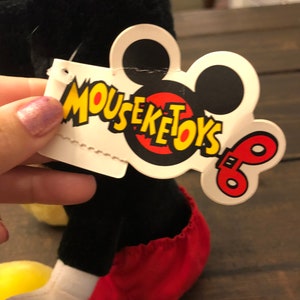 May include: Black and red plush Mickey Mouse toy with a white tag that says "Mouseketoys" with a red and yellow Mickey Mouse head and a red and yellow wind-up key.
