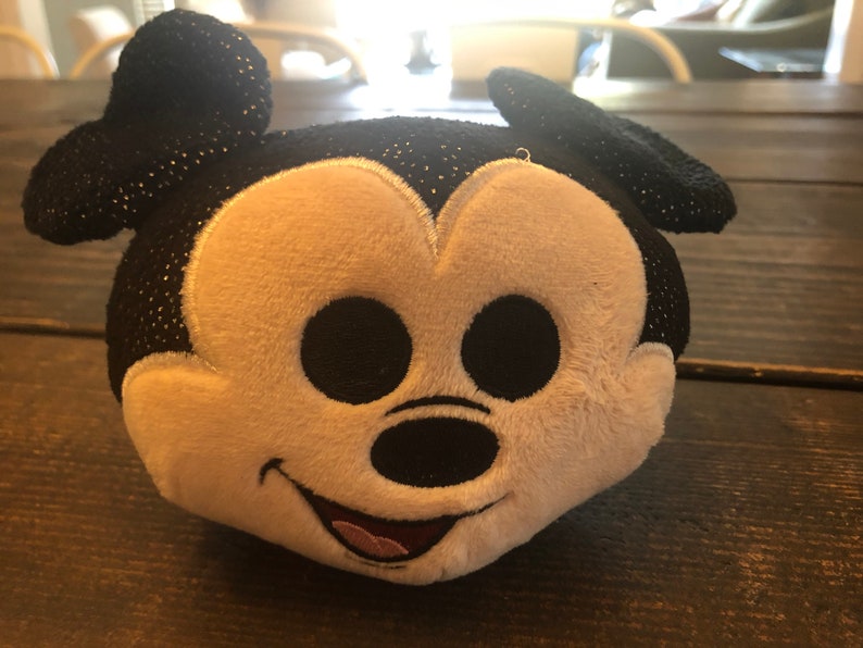 May include: A black and white plush toy of Mickey Mouse with a sparkly black fabric. The toy has a big smile and large black eyes.