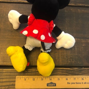 May include: A plush Minnie Mouse toy with black ears, a red dress with white polka dots, and yellow shoes. The toy is about 13 inches tall.