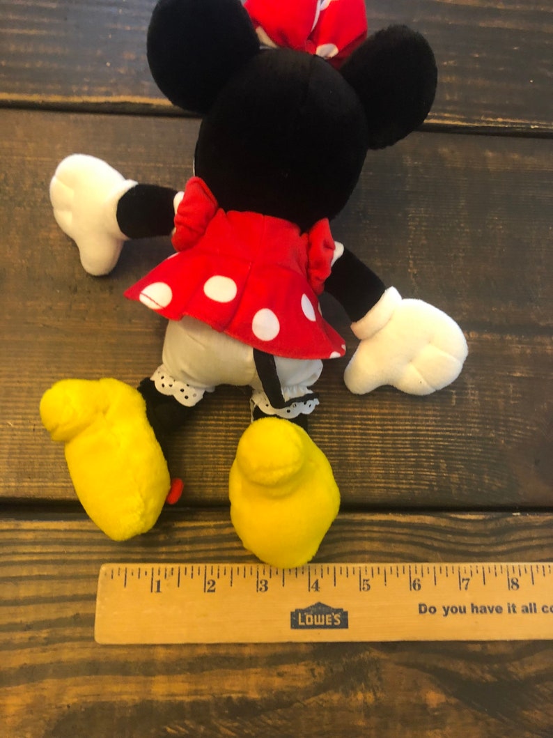 May include: A plush Minnie Mouse toy with black ears, a red dress with white polka dots, and yellow shoes. The toy is about 13 inches tall.