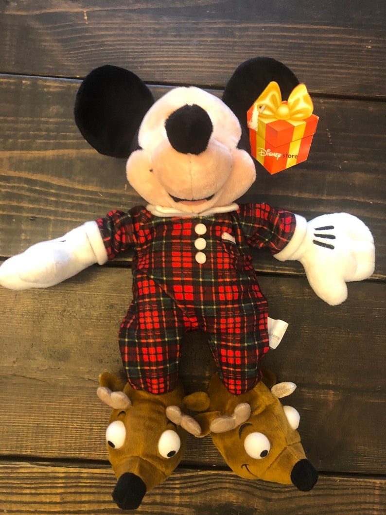 May include: A plush Mickey Mouse wearing red and green plaid pajamas and reindeer slippers. The plush toy has a Disney Store tag attached to its arm.