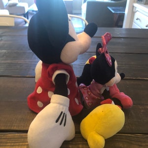 May include: Two plush toys, a red and white polka dot Minnie Mouse and a black and white Minnie Mouse, both wearing red dresses. The Minnie Mouse on the left is holding a yellow plush toy.