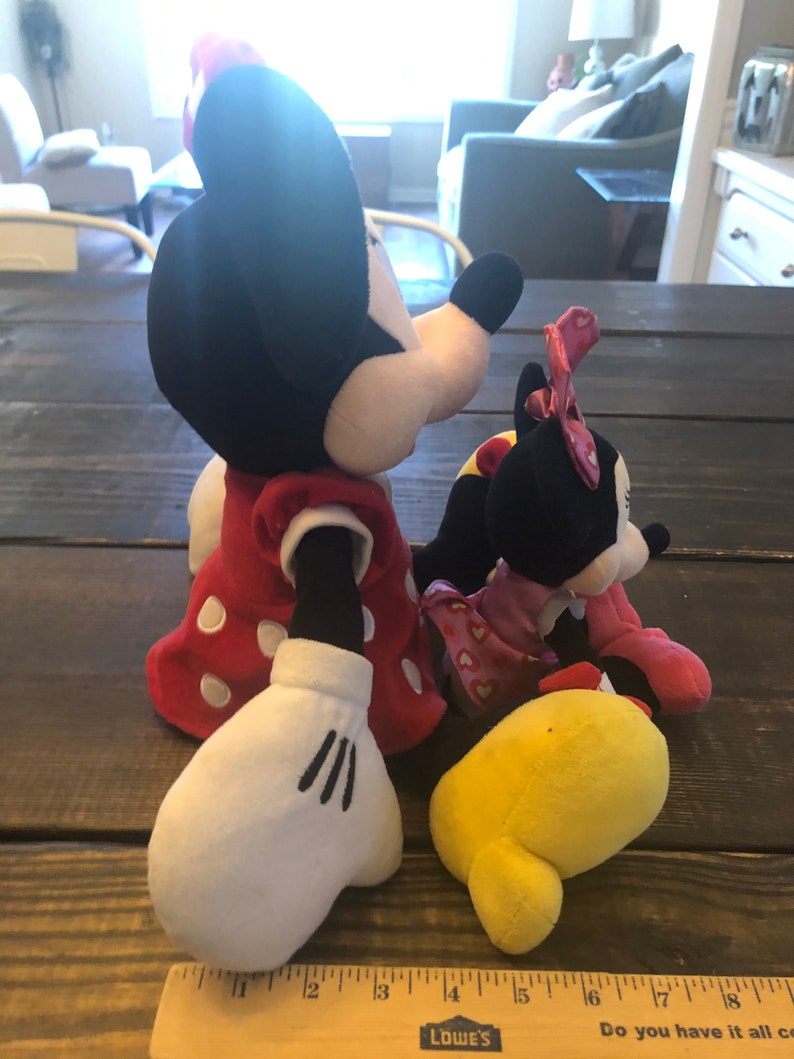 May include: Two plush toys, a red and white polka dot Minnie Mouse and a black and white Minnie Mouse, both wearing red dresses. The Minnie Mouse on the left is holding a yellow plush toy.