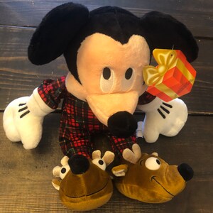 May include: A plush Mickey Mouse wearing red and black plaid pajamas and reindeer slippers. The plush toy has a gift tag attached to its arm that says "Merry Christmas".
