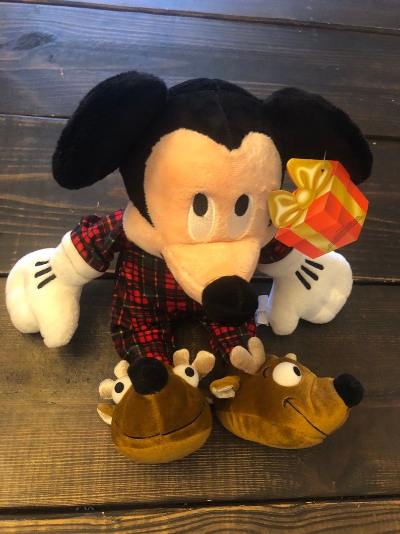 May include: A plush Mickey Mouse wearing red and black plaid pajamas and reindeer slippers. The plush toy has a gift tag attached to its arm that says "Merry Christmas".