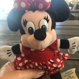 Puede incluir: Un vestido rojo con lunares blancos y un lazo rojo en la cabeza. El peluche es una representaci&oacute;n de Minnie Mouse. La etiqueta dice "Disneyland Walt Disney World &copy;Disney Todos los materiales nuevos de fibra de poli&eacute;ster. Reg. No. PA-1346 (CN) Canad&aacute;. Instrucciones de lavado: lavado en superficie &uacute;nicamente. Producto de China."