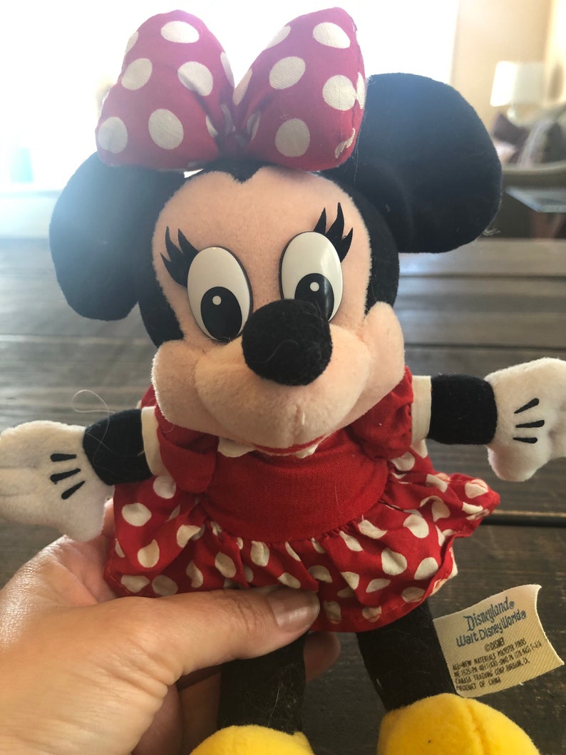 Puede incluir: Un vestido rojo con lunares blancos y un lazo rojo en la cabeza. El peluche es una representaci&oacute;n de Minnie Mouse. La etiqueta dice "Disneyland Walt Disney World &copy;Disney Todos los materiales nuevos de fibra de poli&eacute;ster. Reg. No. PA-1346 (CN) Canad&aacute;. Instrucciones de lavado: lavado en superficie &uacute;nicamente. Producto de China."