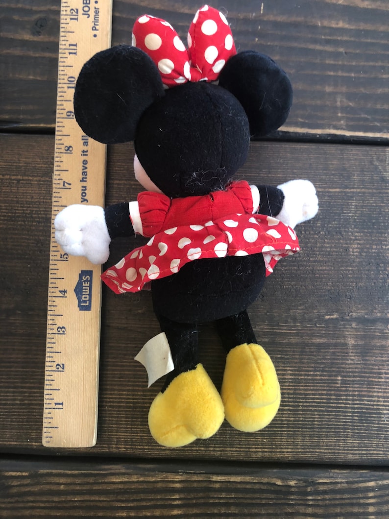 Puede incluir: Un juguete de peluche negro y rojo de Minnie Mouse que lleva un vestido rojo con lunares blancos y un lazo rojo con lunares blancos. El juguete mide aproximadamente 17 cm de alto y tiene zapatos amarillos.
