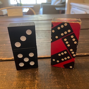 May include: A close-up of two dominoes. One domino is black with white dots and the other is a red box with black and white dominoes printed on it. The box says "Dominoes Decanter" on it.