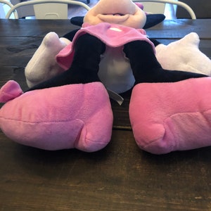 May include: A pink and black plush toy of a cartoon mouse with large feet. The toy is lying on its back with its arms outstretched.