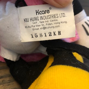 May include: A white, pink, and yellow plush toy with a black tag that reads "Kcare KIU HUNG INDUSTRIES LTD. 14/F., Yale Ind. Centre, 63 Au Pui Wan St., Fotan, Hong Kong. Email: kh@kiuhung.com 15812KH"