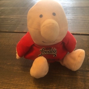May include: A plush toy with a large, pink nose and red shirt. The shirt has the text "Lovable" printed on it in a white, cursive font.