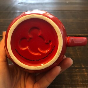May include: Red ceramic mug with a Mickey Mouse silhouette on the bottom. The mug says "Microwave/Dishwasher Safe Hallmark Cards, Inc."