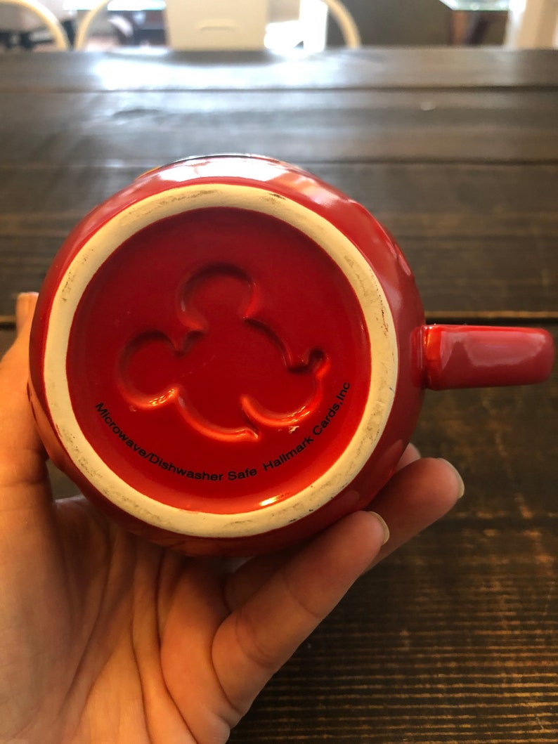 May include: Red ceramic mug with a Mickey Mouse silhouette on the bottom. The mug says "Microwave/Dishwasher Safe Hallmark Cards, Inc."