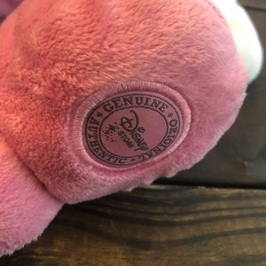 May include: A pink plush toy with a brown embroidered tag that reads "Genuine * Disney Store * Authentic * Original".