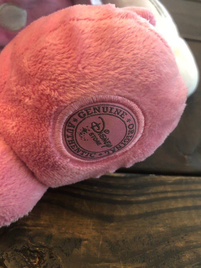May include: A pink plush toy with a brown embroidered tag that reads "Genuine * Disney Store * Authentic * Original".