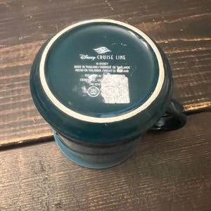 May include: A teal ceramic mug with a white rim, featuring the "Disney Cruise Line" logo and text. The mug is made of stoneware and has a capacity of 16 oz. The mug is teal with a white rim and a black handle.
